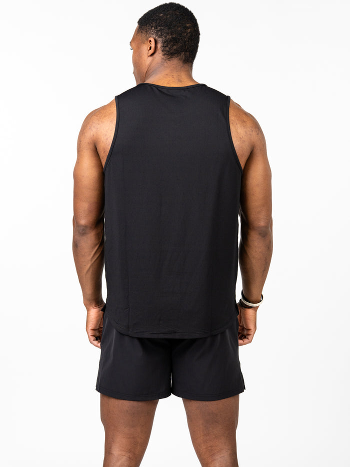 Man wearing a black Signature Tank, standing with back to camera in a plain white studio, dressed in black athletic shorts showcasing breathable, 4-way stretch performance fabric suitable for intense training.