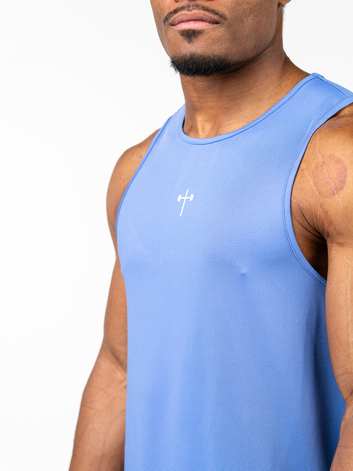 Athletic man wearing a blue Signature Tank designed for intense training, featuring a small white Christian cross with a barbell icon on the chest, made from breathable performance fabric.