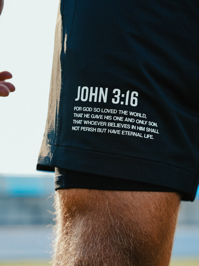 Person wearing black shorts with 'John 3:16' text, standing outdoors.