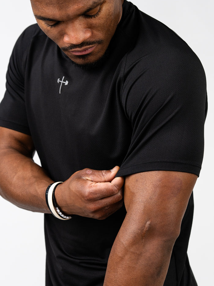 Man wearing a black Signature Tee with a small Christian cross and barbell logo on the chest, showing the breathable, stretch fabric suited for intense training and workouts.