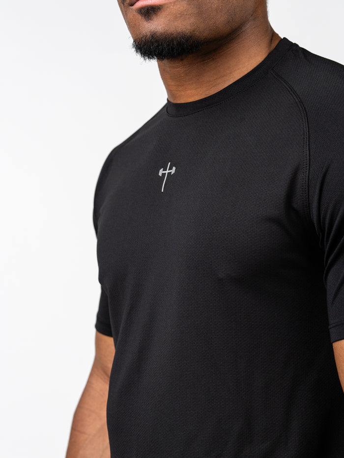 Man wearing a black Signature Tee featuring a small Christian cross with a barbell design on the chest, made from breathable, moisture-wicking performance fabric.