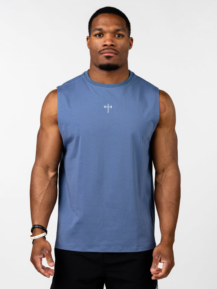 A muscular man wearing a blue Vital Cross Sleeveless Tank featuring a small white Christian cross with a barbell design on the chest, styled as Christian gym clothing for high-intensity workouts.