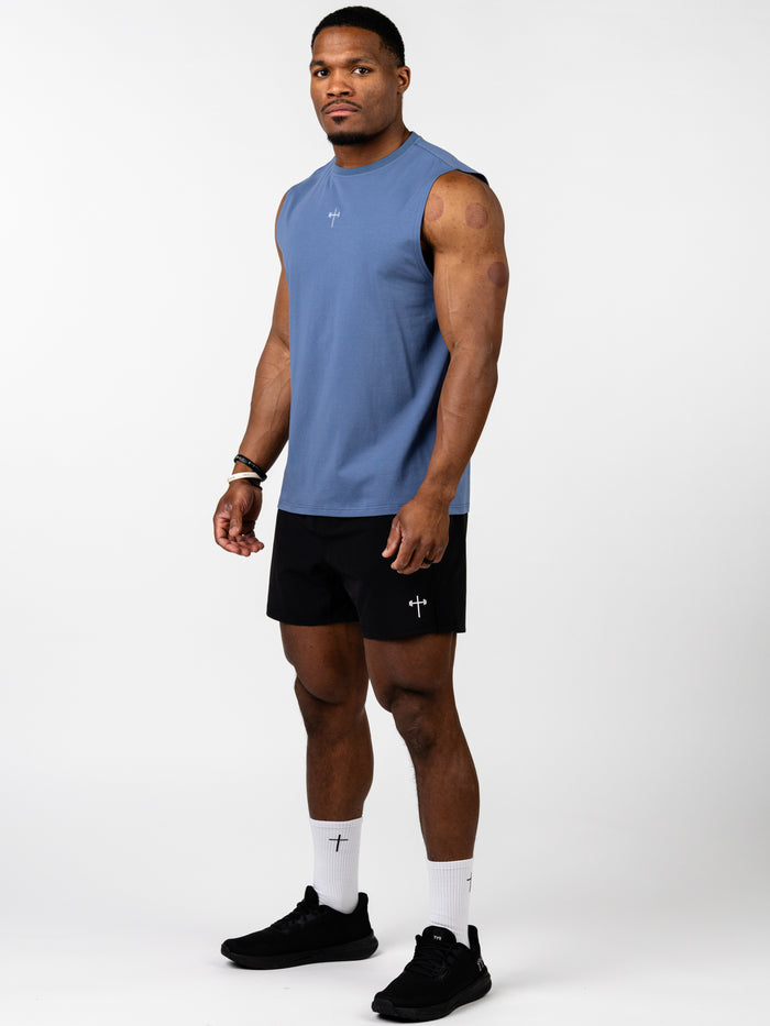 Athletic man wearing a blue Vital Cross Sleeveless Tank paired with black shorts, showcasing Christian fitness apparel designed for high-output training and unrestricted movement.