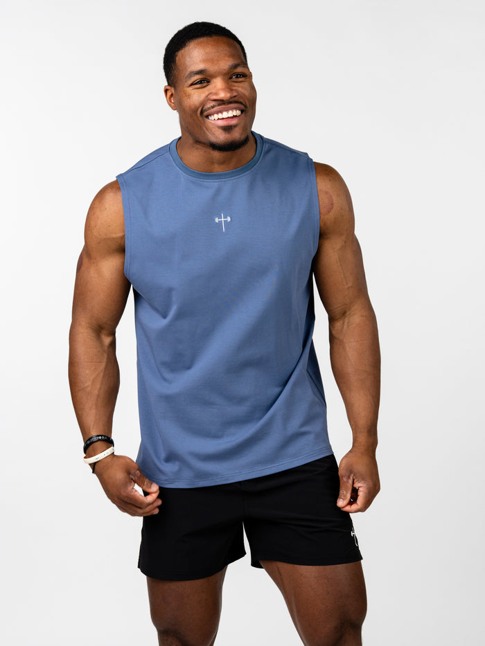 Athletic man wearing a blue Vital Cross Sleeveless Tank designed for high-output training, featuring a minimalist Christian cross and barbell design on the chest.