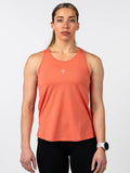 Woman wearing a coral Women's Signature Tank featuring a small white cross with a barbell design on the chest, paired with black leggings and a white fitness watch.