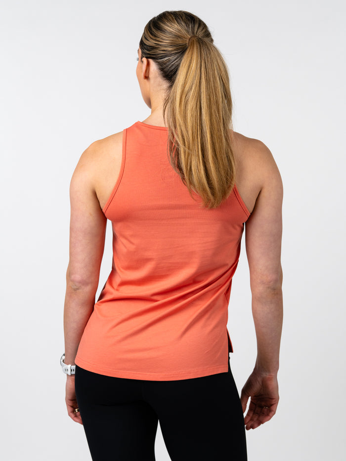 Woman wearing a coral-colored Women's Signature Tank made from soft cotton-spandex blend, shown from the back, paired with black leggings in a fitness setting.
